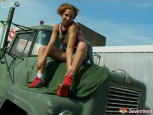 Curly redhead babe stips seductively sitting on hood of a huge truck